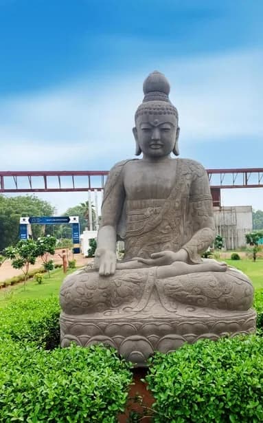 Stone seated Buddha sculpture on a landscaped lawn near the entrance to the Sector 88A development, with a road-sign gantry and construction behind.