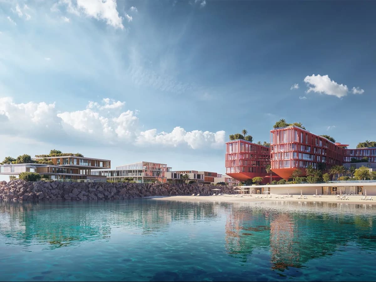 Render from the sea of the Mira Coral Bay shoreline with red-facade hotel buildings, terraced villas on a rocky headland and a sandy beach