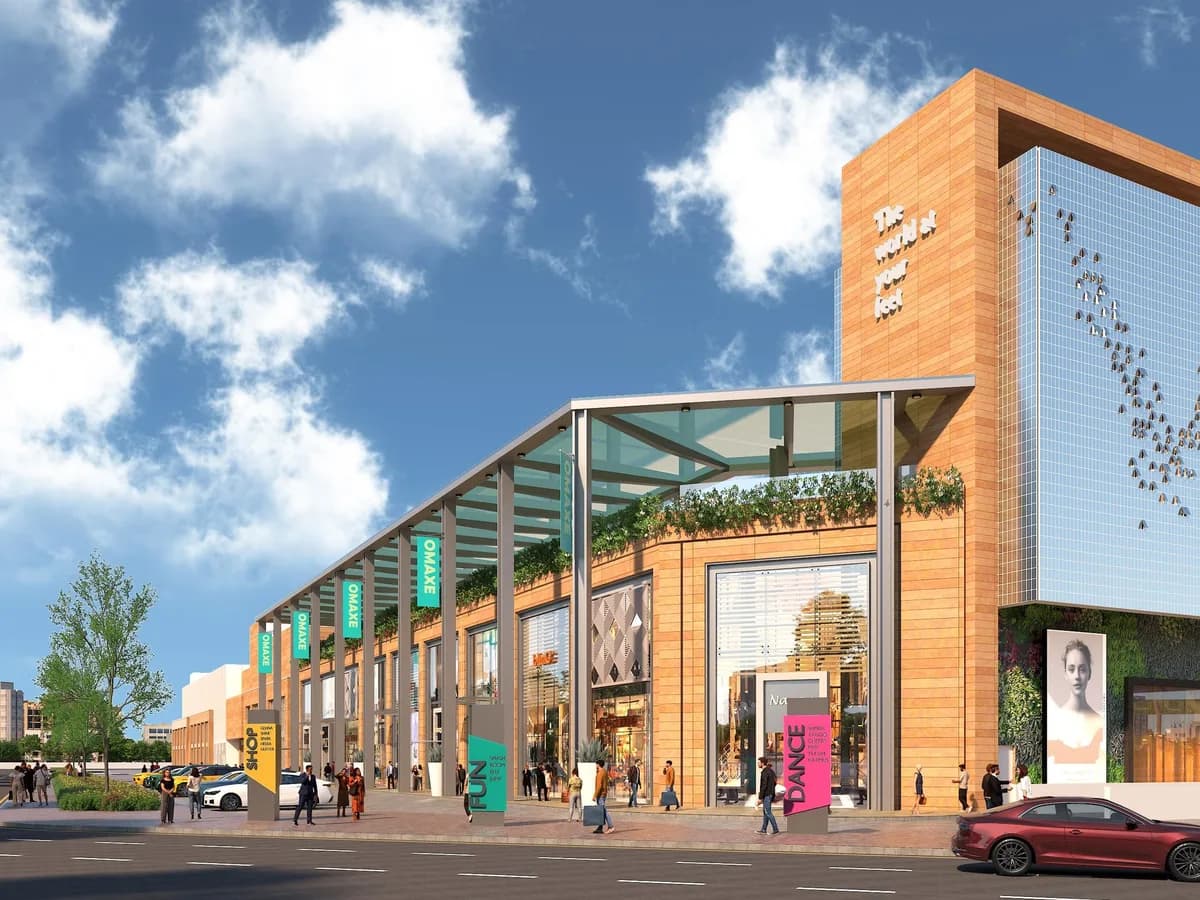 Daytime render of a two-storey retail frontage with a glass canopy, Omaxe banners and a tower reading 'The world at your feet'
