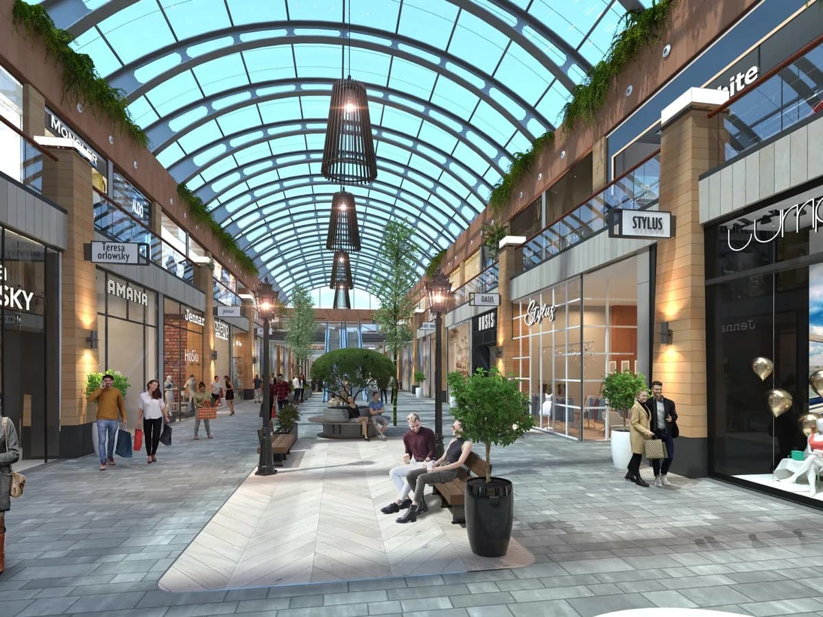 Render of the air-conditioned high street interior: a glass-vaulted shopping street with two levels of shops, pendant lights, benches and shoppers