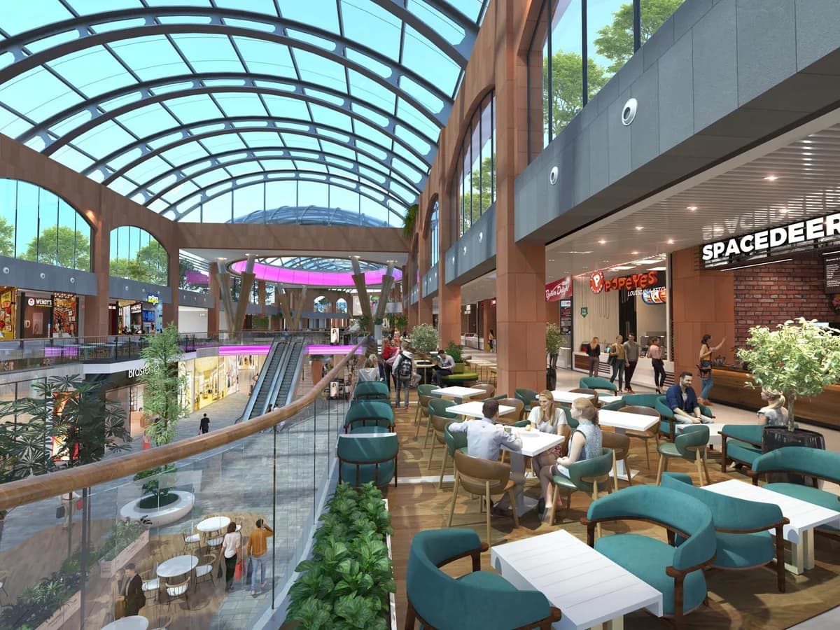 Render of an upper-level food court under a glass vaulted roof, with café seating overlooking the shopping street below