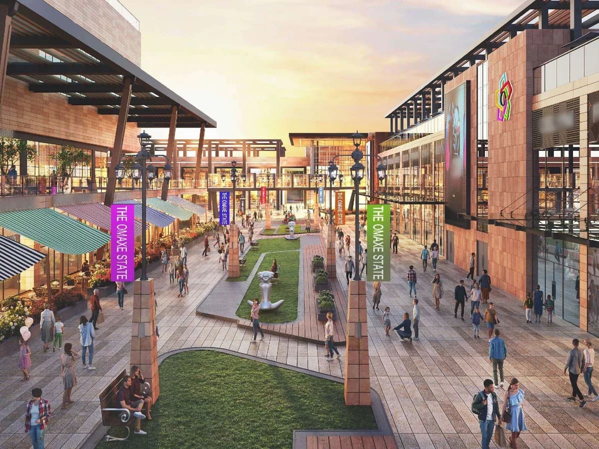 Sunset render of the Social District promenade: a landscaped lawn with sculptures between two-level shopfronts, awnings and 'The Omaxe State' banners